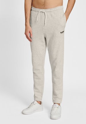 Pantalons de survêtement gris clair avec une taille élastique et un cordon de serrage, présentant un petit logo noir sur la cuisse gauche et des chevilles fuselées.