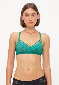 Green mesh bralette with a v-neck, featuring geometric patterns, adjustable straps, layered design, and a smooth finish.