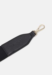 Extrémité de sangle de sac en cuir noir texturé avec un fermoir à pince homard en métal doré sur fond blanc.