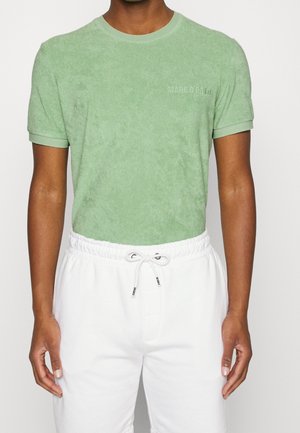 Mężczyzna ubrany w jasnorozową bawełnianą koszulkę z krótkim rękawem z napisem "MARC O'POLO" oraz białe spodnie dresowe ze sznurkiem.