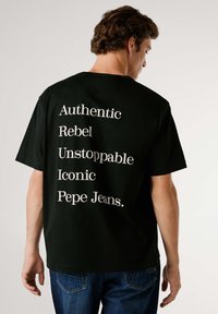 Camiseta negra de algodón con texto blanco en la espalda: "Auténtico, Rebelde, Imparable, Icónico, Pepe Jeans." Manga corta, corte holgado.