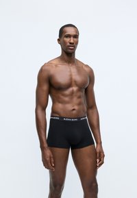 Melnas bokseru bikses, kas izgatavotas no mīkstas auduma ar pieguļošu dizainu. Aprīkotas ar melnu jostu, uz kuras redzams balts "BJÖRN BORG" zīmols.