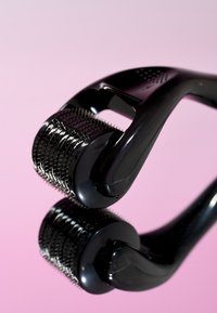 Zwarte dermaroller met een gestructureerd handvat en een cilindrische roller bedekt met fijne metalen naalden, reflecterend op een roze achtergrond.