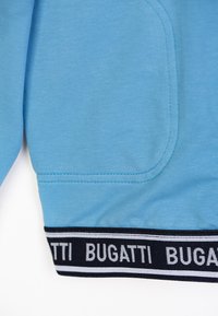Felpa azzurra chiara con una trama liscia, una tasca laterale e una vita elastica nera con la scritta ripetuta "BUGATTI".