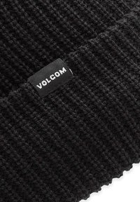 Schwarze Strickmütze mit strukturiertem Muster, ausgestattet mit einem schwarzen Etikett mit weißem "VOLCOM"-Text. Weiches, elastisches Material.