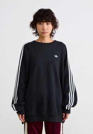 Sort oversized sweatshirt lavet af blødt stof, med hvide tre-stribe accenter på ærmerne og et lille hvidt logo på brystet.