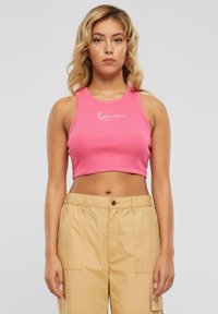 Rosa ribbet cropped tank top med rund hals og hvit logo detalj foran, kombinert med beige høy-halsbukser.