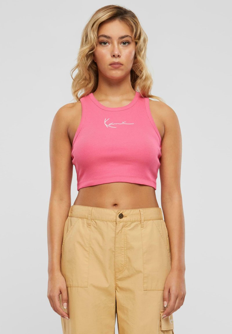 Rosa ribbet cropped tank top med rund hals og hvit logo detalj foran, kombinert med beige høy-halsbukser.