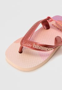 Ružová šľapka s lesklým, tmavoružovým pásikom, textúrovanou stélkou a logom "havaianas"; určená na každodenné nosenie.