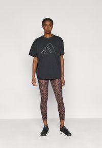 Μαύρο φαρδύ t-shirt με λευκό λογότυπο Adidas, συνδυασμένο με κολάν με λεοπάρ σχέδιο σε αποχρώσεις του καφέ και μαύρα αθλητικά παπούτσια.