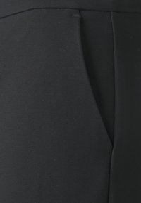 Black pants made from soft fabric, featuring a smooth texture, streamlined design, and a discreet side pocket detail.