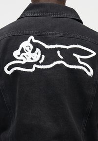 Μαύρο τζιν μπουφάν με μεγάλο λευκό γραφικό ενός σκύλου που πηδά στην πλάτη. Απλός γιακάς και παραδοσιακές ραφές.