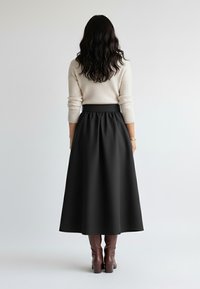 Czarna spódnica sięgająca do podłogi o gładkiej fakturze z elastycznym paskiem w talii, zestawiona z brązowymi kozakami za kolano i kremowym, prążkowanym swetrem.