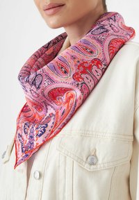 Zijden sjaal met een levendig paisleypatroon in roze, rood en paarse tinten, los om de hals gedragen, tegen een crème jasje.