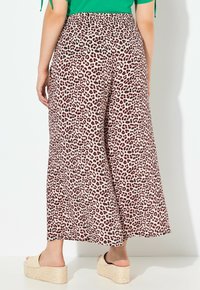 Leopardmuster weit geschnittene Hose in einem hellrosa Farbton, mit hoher Taille und weichem Stoff. Kombiniert mit beigen Keilsandaletten.