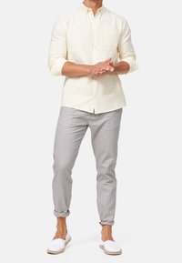 Koszula w kremowym kolorze z krótkim rękawem i kołnierzykiem na guziki, szare dopasowane spodnie oraz białe espadryle. Prosty design bez wzorów.