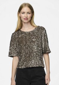 Top marrón con lentejuelas y mangas cortas; presenta un corte holgado y un escote redondo; superficie texturizada con detalles brillantes. Lo lleva puesto con pantalones negros.
