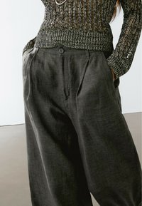 Dunkelgraue Leinen-Hose mit weitem Bein, faltig an der Vorderseite und mit einen Knopfverschluss, seitlichen Taschen und einer weichen, strukturierten Oberfläche.