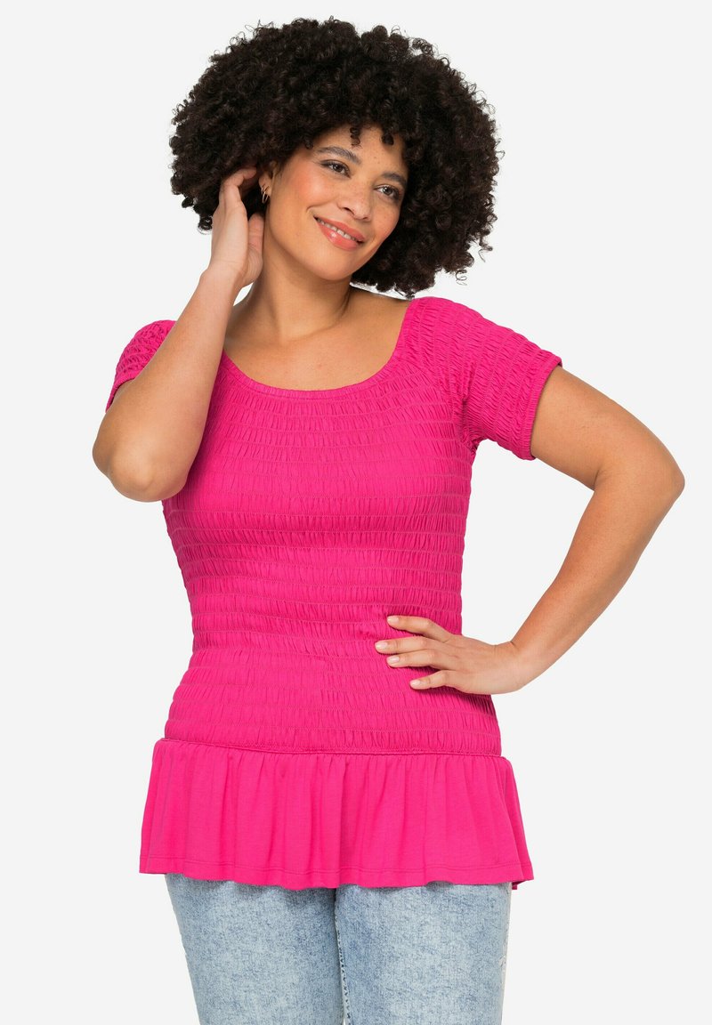 Top fucsia con fruncidos, de mangas cortas, escote cuadrado y dobladillo acampanado, combinado con vaqueros de lavado claro. Textura suave, ajuste casual.