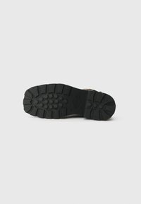 Black rubber sole with deep tread patterns and circular accents, featuring a textured surface for grip. Flat design with durable construction.