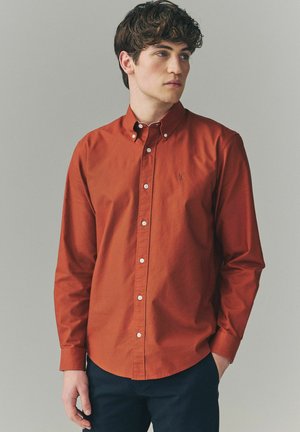 Long-sleeve, button-down shirt in rust-orange cotton, featuring a classic collar, white buttons, and a small logo on the chest.