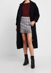 Sort lang frakk, burgunder sweater og grå plaid mini-nederdel med volangkant. Sorte ankelstøvler med lynlåsdetalje.