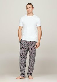 Hvid crew-neck t-shirt kombineret med sorte pyjamabukser med røde og hvide tekstmønstre. Let stof; lige skåret bukser med åben kant.
