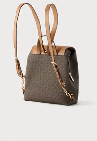 Ruskeakuvioinen kangaslaukku vaaleanruskeilla nahkaosilla, kaksilla olkahihnoilla ja kultasävyisellä vetoketjulla yhdellä sivulla.