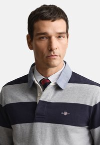 Polo riscada em cinza e azul-marinho, com gola em ganga, pala com três botões e logótipo no peito. Tecido de algodão texturado.