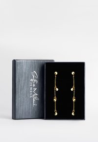 Guldtonade örhängen med hängande kedjor och sfäriska detaljer, visade i en texturerad svart presentlåda med vitt logotyp.