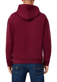 Felpa bordeaux con cappuccio, polsini e orlo a coste. Tessuto morbido; abbinata a jeans blu scuro con cuciture a zigzag sui taschini.