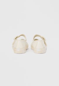 Chaussures beige clair avec une texture scintillante, dotées d'une sangle arrière et de semelles en caoutchouc. Design arrondi avec des accents minimalistes.