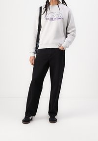 Jasnoszary sweatshirt z kolorowym napisem "ALPHA STUDIO EDITION", zestawiony z luźnymi czarnymi spodniami i czarnymi sneakersami.