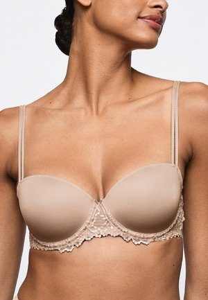 Close-up of a woman wearing a beige padded bra with lace trim and adjustable straps, showing her neck and upper chest.
