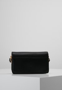 Černá kožená crossbody taška s klopou, zlatými kovovými detaily a hladkým povrchem. Kompaktní obdélníkový tvar s prošitými detaily.