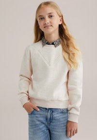 Felpa rosa chiaro con un design a chevron cucito e dettagli in strass, indossata sopra una camicia con colletto a stampa leopardata. Vestibilità comoda, polsini a costine.