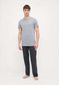T-shirt en coton gris à manches courtes assorti à un pantalon de pyjama à carreaux noir et gris, tous deux à coupe décontractée, présentés sur un modèle masculin debout.