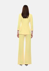 Completo giallo composto da un blazer aderente e pantaloni a gamba larga, realizzato in tessuto morbido. Il blazer ha maniche a tre quarti e una silhouette su misura.