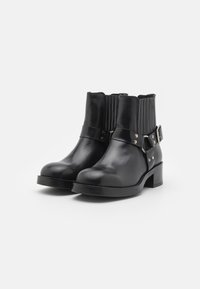 Black leather ankle boots with ribbed elastic sides, metal buckle accents, and a low block heel. Smooth texture, rounded toe design.