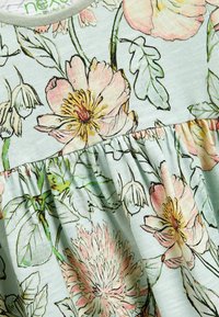 Robe florale avec un fond bleu clair, ornée de fleurs pêches et jaunes. Détail de jupe froncée avec des feuilles vertes et une texture de tissu douce.