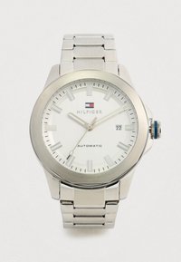 Silver Tommy Hilfiger wristwatch with white face, silver hour markers, date display showing 22, and metal link band.