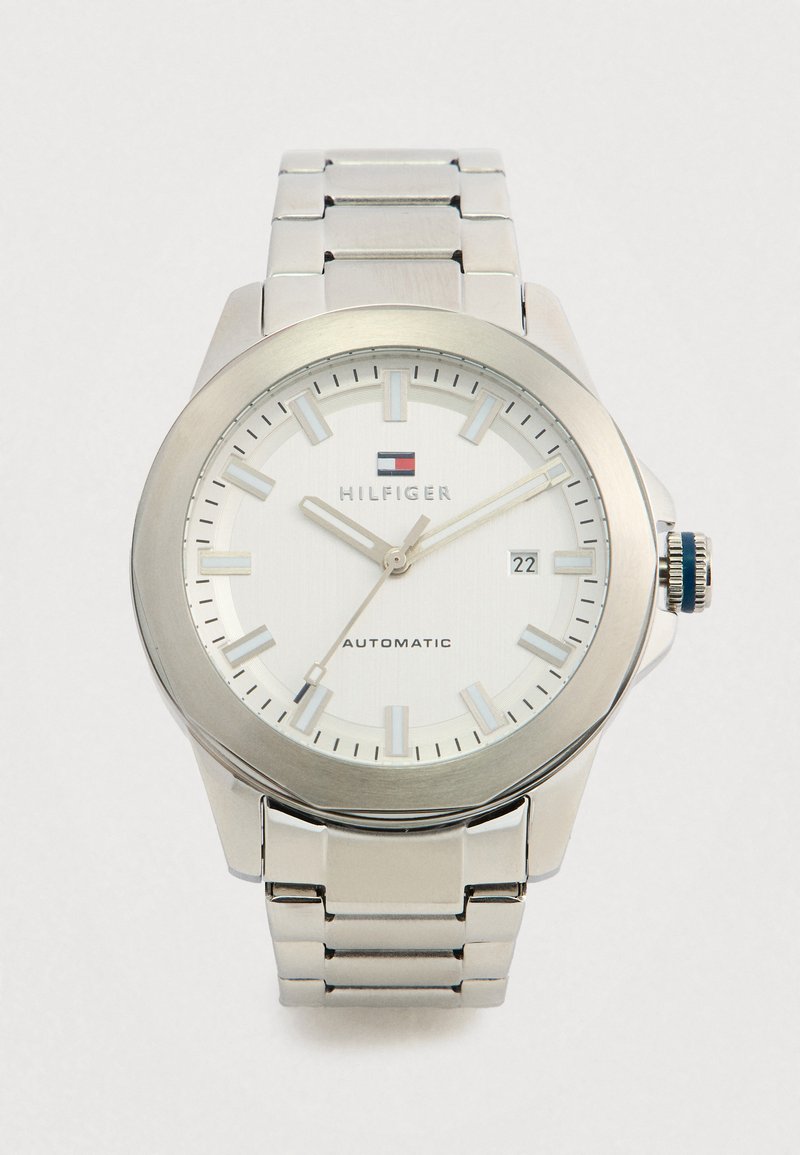 Silver Tommy Hilfiger wristwatch with white face, silver hour markers, date display showing 22, and metal link band.