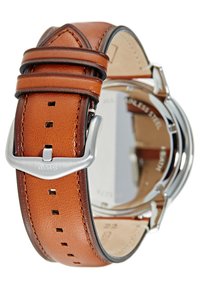 Bracelet de montre en cuir marron avec boucle en argent, attaché à un boîtier de montre en acier inoxydable, vu de l'arrière.