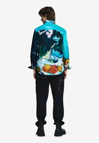 Farebná košeľa na zapínanie s potlačou zátišia na tyrkysovom pozadí, kombinovaná s tmavými cargo nohavicami a čiernymi čižmami.