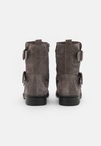 Botas de ante gris hasta el tobillo con dos hebillas laterales, tacón negro apilado y punta redonda lisa. La vista trasera muestra un acabado de ante texturizado.
