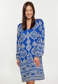 Rochie albastră cu mâneci lungi, de tip V, prezentând modele florale albe și accente geometrice. Material ușor, cu o croială lejeră.