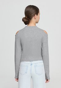 Maglietta grigia a maniche lunghe con dettagli sulle spalle a taglio, realizzata in morbido tessuto. Abbinata a jeans in denim chiaro, caratterizzati da un design semplice.