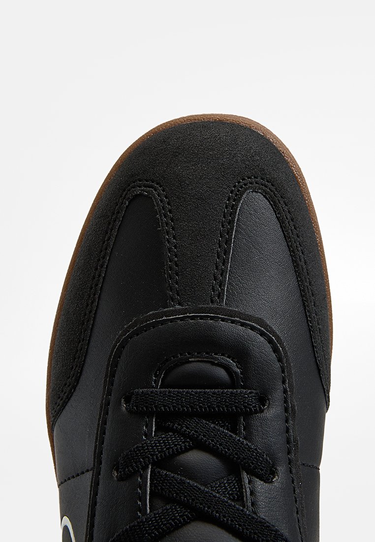 Baskets noires avec des panneaux en daim et en cuir, lacets noirs et une semelle en caoutchouc brun, montrées en vue rapprochée de face et de dessus.