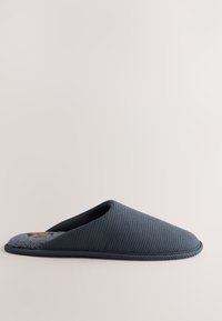 Sötétkék, texturált, bebújós papucs puha szürke gyapjúbéléssel és lapos talppal, világos háttéren.