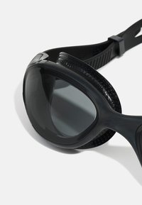 Lunettes de natation noires avec un design incurvé, des verres teintés foncés, des accents texturés et une sangle ajustable pour un maintien sécurisé.
